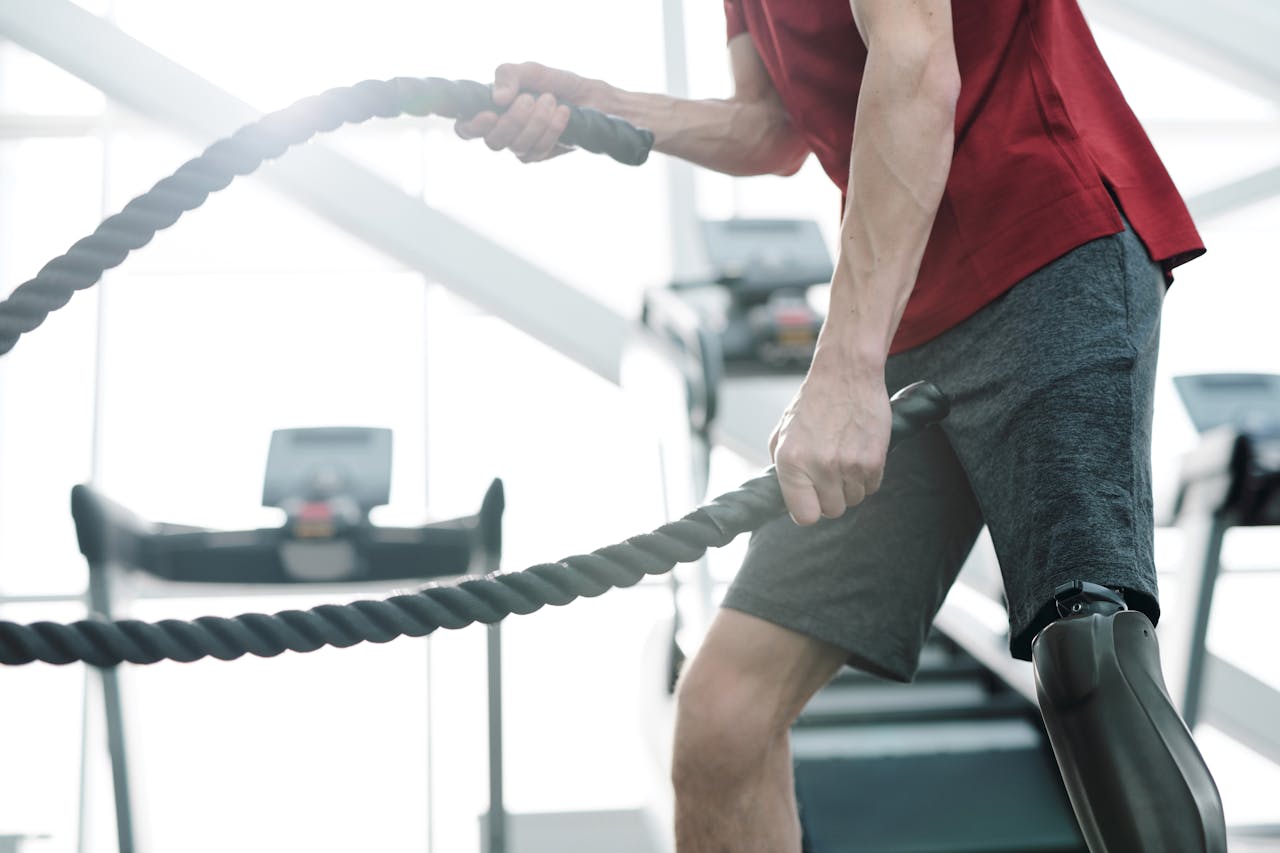 Close-up of a man with a prosthetic leg working out with battle ropes at the gym.